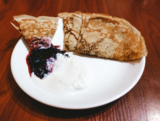 Appetizing fried pancakes with sour cream and jam on a white plate