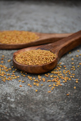 Fenugreek seeds in wooden spoon on textured background