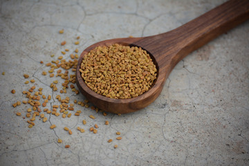 Fenugreek seeds in wooden spoon on cracked concrete texture background