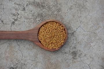 Fenugreek seeds in wooden spoon on cracked concrete texture background