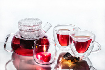 Tea for two in heart mugs with a burning heart-shaped candle in a transparent candlestick on a glass table with reflection with a slice of chocolate