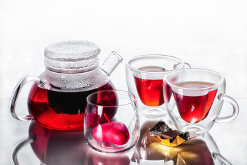 Tea for two in heart mugs with a heart-shaped candle in a transparent candlestick on a glass table with reflection with a slice of chocolate