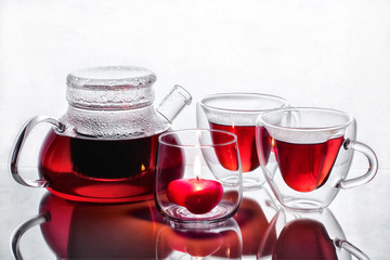 Tea for two in mugs of hearts with a burning candle in the shape of a heart in a transparent candlestick on a glass table with reflection