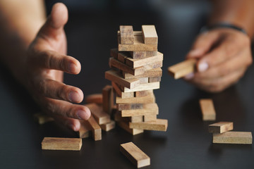 Engineer hand cover wooden block and piling up and stacking a wooden block tower on black desk. planning, risk and strategy in business concept.