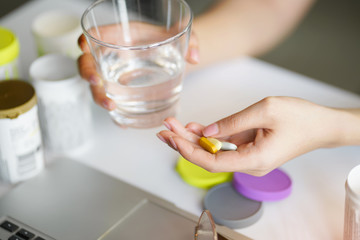 Office women pouring the pills vitamin,supplements out of the bottle on hand and holding a glass of water at home office.Healthcare and medicine concept. selective focus