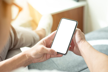 Mockup image blank white screen cell phone.man hand holding texting using mobile on sofa at home office.background empty space for advertise text.people contact marketing business,technology