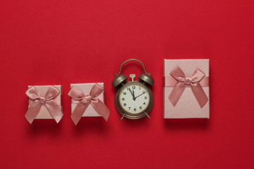 Retro alarm clock and gift boxes with bow on red background. 11:55 am. New Year, Christmas.concept. Top view