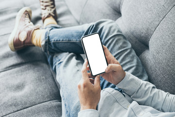 Mockup image blank white screen cell phone.man hand holding texting using mobile on sofa at...