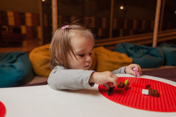 Naklejka premium Little girl plays toy bricks at table in children's entertainment center