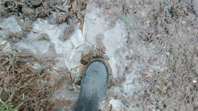 Looking down at someone wearing boots cracking an icy puddle, handheld