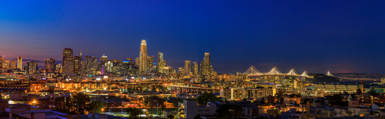 Fototapeta na wymiar San Francisco skyline night panorama with city lights, the Bay Bridge and trail lights