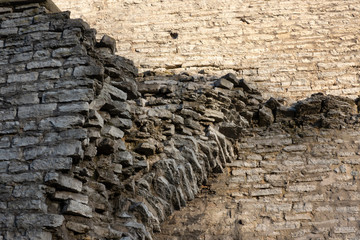 Wall of an old fortress made of gray stone blocks. A fragment of the structure is destroyed. You can see the fault point with protruding stones. Background. Texture.