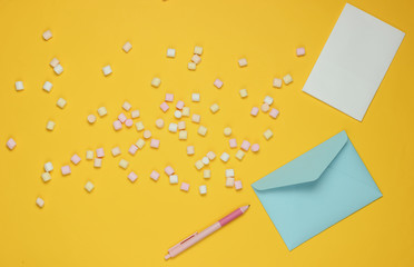 Blue Envelope with pen and marshmallows.on yellow background. Flat lay mockup for valentines day, wedding or birthday. Top view