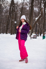 Portrait of a young beautiful woman in a ski suit posing in winter park