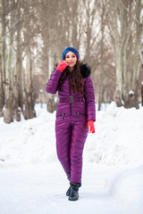 Fototapeta na wymiar Portrait of a young beautiful woman in a ski suit posing in winter park
