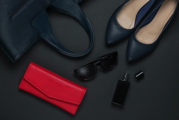 Women's accessories on a black background. High heel shoes, leather bag, purse, sunglasses, perfume bottle. Top view