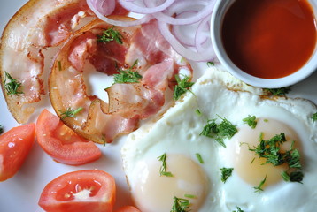 Fried eggs with tomatoes, red onion, bacon for breakfast on a white plate on the black background. Delicious homemade breakfast.