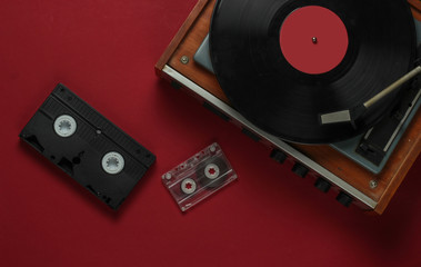 Flat lay retro media and entertainment. Vinyl record player with vinyl record, audio cassette, vhs on red background. 80s. Top view