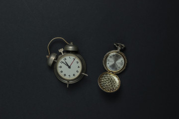 Retro alarm clock and pocket watch on black background. 11:55 am. New Year.