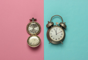 Retro alarm clock and pocket watch on pink blue pastel background. 11:55 am. New Year.
