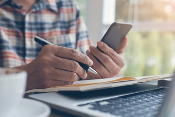 Man working on laptop computer and using smart phone in cafe