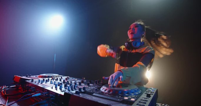 Cool female asian dj is working in a nightclub, standing at turntables, creating a dance music set - nightlife concept 4k footage