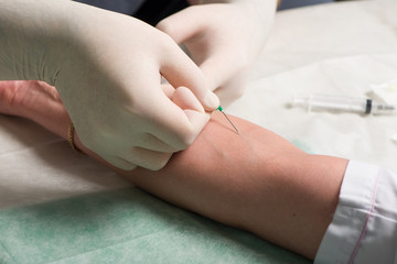 Hands in medical gloves perform vein puncture in area of ulnar bend of patient 's hand