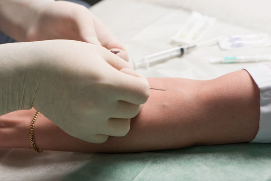 Hands in latex medical gloves perform vein puncture in ulnar bend of patient 's hand