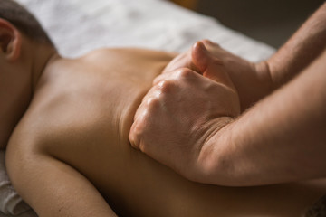 Boy toddler relaxes from a therapeutic massage. Physiotherapist working with patient in clinic to the back of a child