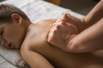 Boy toddler relaxes from a therapeutic massage. Physiotherapist working with patient in clinic to the back of a child