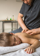 Boy toddler relaxes from a therapeutic massage. Physiotherapist working with patient in clinic to the back of a child