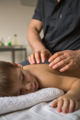 Obraz na płótnie Canvas Boy toddler relaxes from a therapeutic massage. Physiotherapist working with patient in clinic to the back of a child