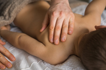Boy toddler relaxes from a therapeutic massage. Physiotherapist working with patient in clinic to the back of a child