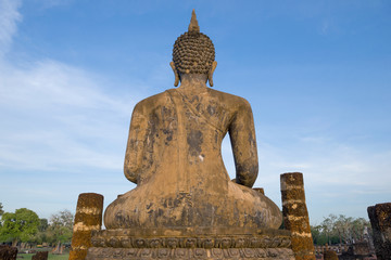 View from the back of ancient sculpture of a sitting Buddha against  blue sky. Sukhothai, Thailand