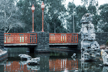 A small local park with red Chinese-style decoration. A lake with decorative stones and stone column. Shepparton, Australia.