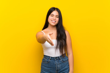 Young teenager Asian girl over isolated yellow background shaking hands for closing a good deal