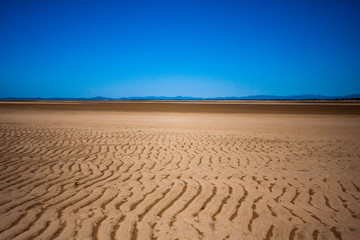 The coastal strip (coastline, beach) at low tide. A wide strip of desert sand to the horizon, a desert area, a wavy relief runs along it. Makey, Queensland, Australia.