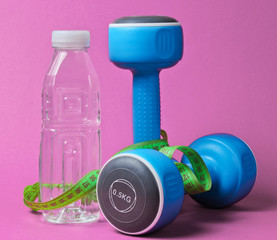Healthy lifestyle still life. Dumbbells, ruler,  bottle of water on pink background. Slimming...