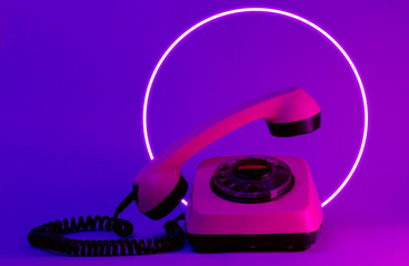 Old style rotary telephone with soaring telephone handle. 80's synth wave and retrowave glowing...