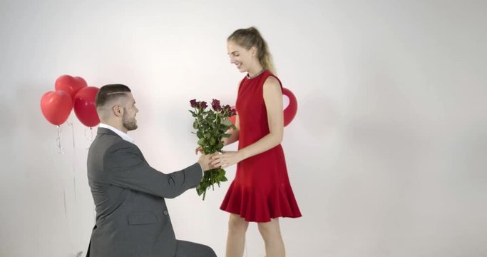 Young couple lover male and beautiful female dress in red are in loving emotion proposing her for marry by show her a red rosses flower and wedding ring and selfie.
