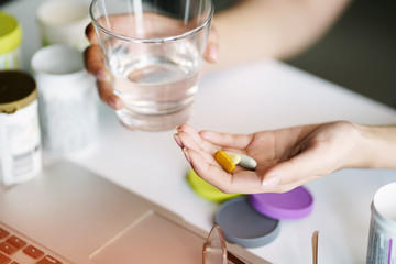 Fototapeta na wymiar women pouring the pills vitamin,supplements out of the bottle on hand and holding a glass of water at home office.Healthcare and medicine concept. selective focus