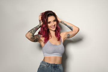 Beautiful woman with tattoos on body against light background