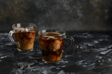 Ice coffee in a glass cups with cream poured over and coffee beans . Cold summer drink on a dark background with copy space for text..