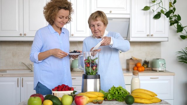 Granddaughter Cooking Smoothie On Kitchen With Grandmother