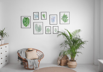 Beautiful paintings of tropical leaves on white wall in living room interior