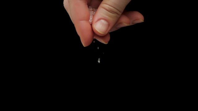 Closeup slow motion of hand of chef cooking food and adding white coarse salt to dish against black background