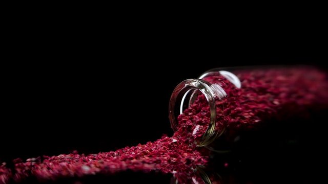 Slow motion of glass pot filled with granules of sumac falling and spilling on mirror surface with black background
