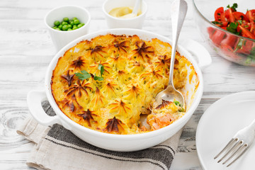 Fish pie with salmon, mashed potatoes, green peas and creamy sauce. on white wooden background