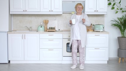 Fototapeta na wymiar Happy Elderly Woman Dancing In Kitchen. Funny Grandmother.