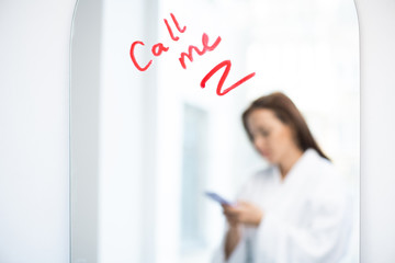 Fototapeta premium Part of mirror with asking for call written with lipstick and reflection of girl